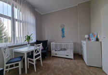  Zdjęcie pokazujące wyposażenie pokoju w Domu dla matek z małoletnimi dziećmi i kobiet w ciąży w Dobieszczyźnie. Z prawej strony znajduje się szafka na której znajdują się lampka oraz obrazek. Obok znajduję się łóżeczko, fotel oraz stolik